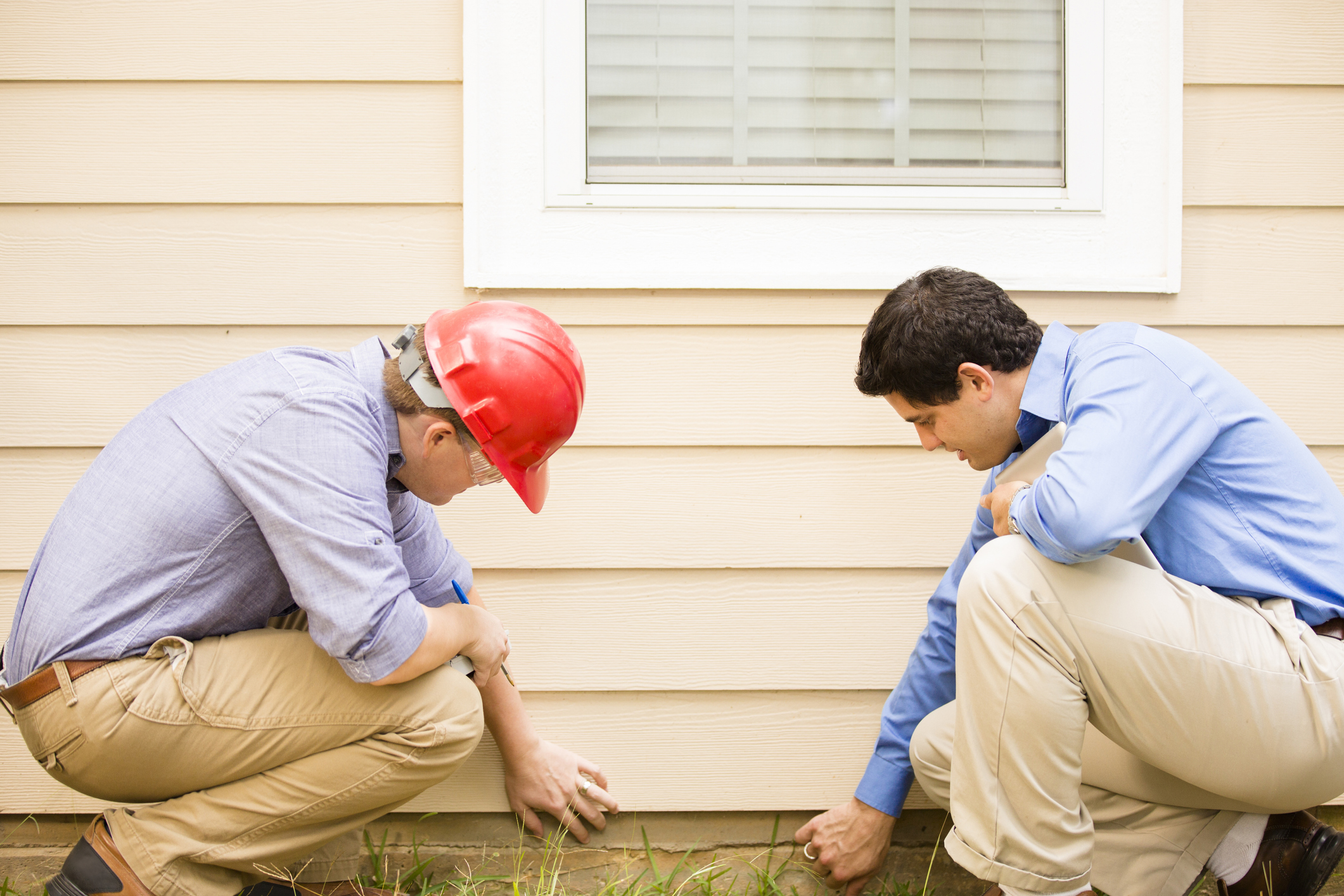 Inspectors or blue collar workers examine building wall, foundation. Outdoors.