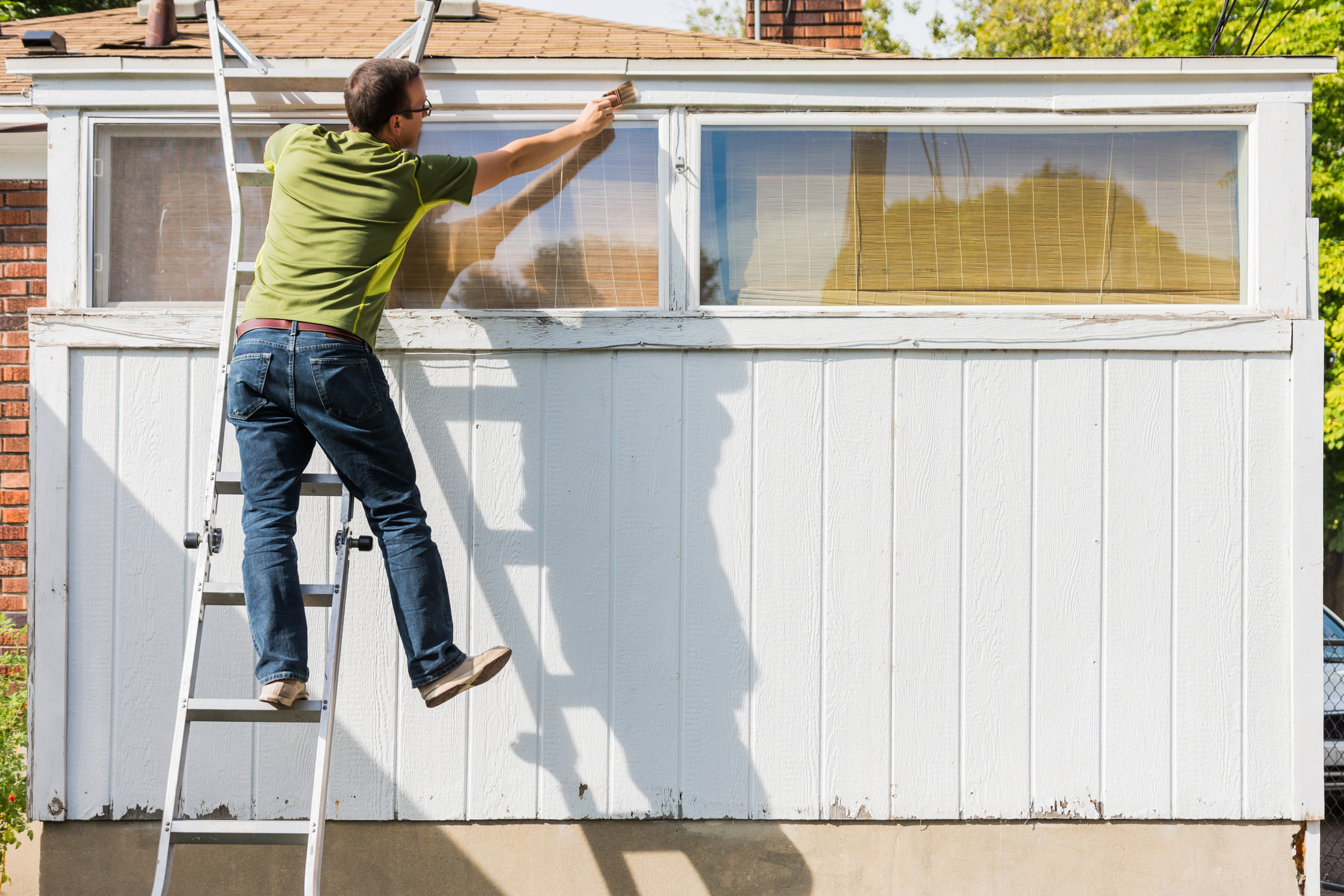 Man reaching to paint white trim on ladder