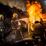 Firefighters spraying water on burning car